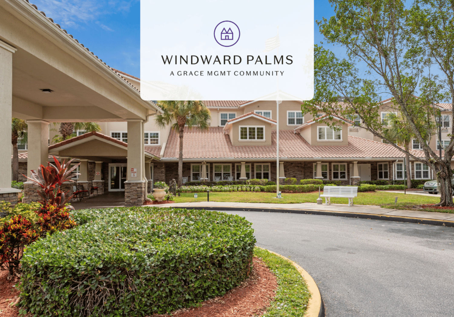 Front view of Windward Palms retirement community with a tiled-roof building, palm trees, and a curved driveway in the foreground.